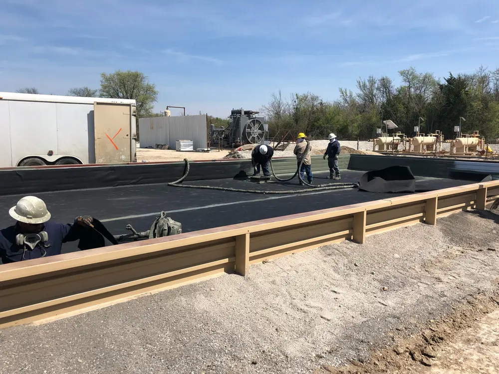 Crew applying spray-on liner coating inside a lined containment berm